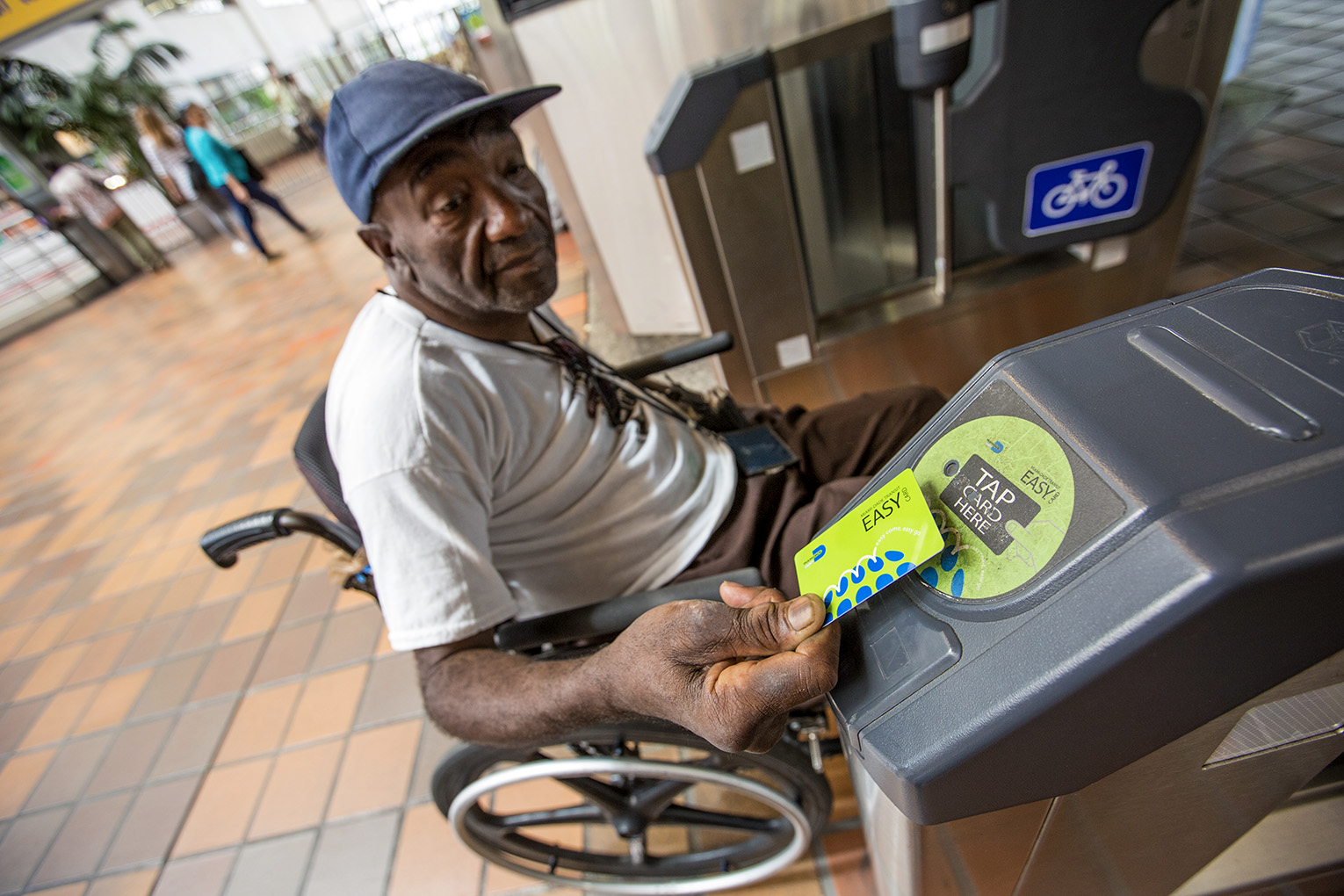 Elderly man in wheel chair using a smart card to pass through a fare gate